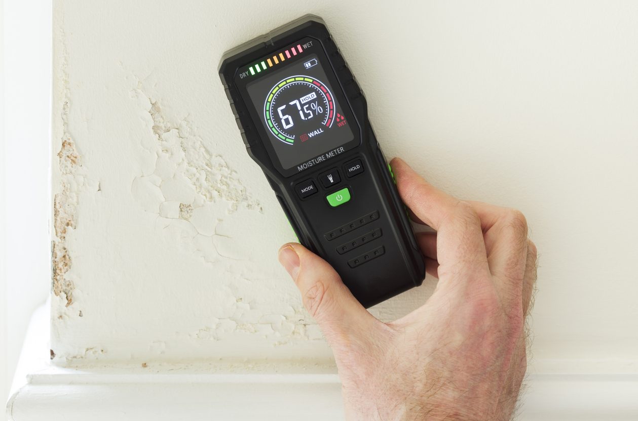 Home inspector using a moisture meter on a wall showing paint bubbling from hidden moisture